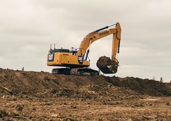 A yellow Caterpillar excavator from Professional Excavators and Construction scoops dirt on a construction site under a cloudy sky, with piles of earth surrounding the machine. - Professional Excavators & Construction